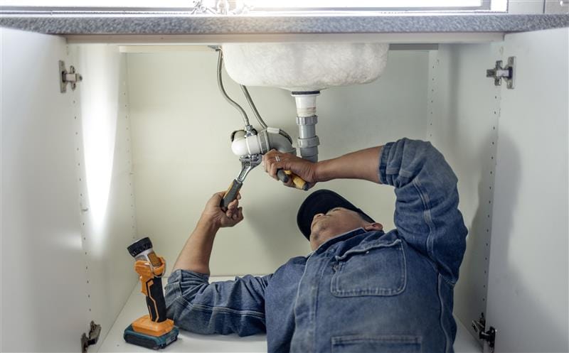 Plumber repairing pipes beneath a bathroom sink in Calhoun