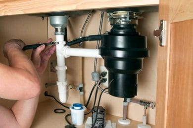 Plumber repairing a garbage disposal beneath a kitchen sink in Calhoun