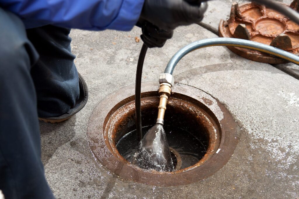 Plumber hydro jetting a sewer line through a manhole in Calhoun