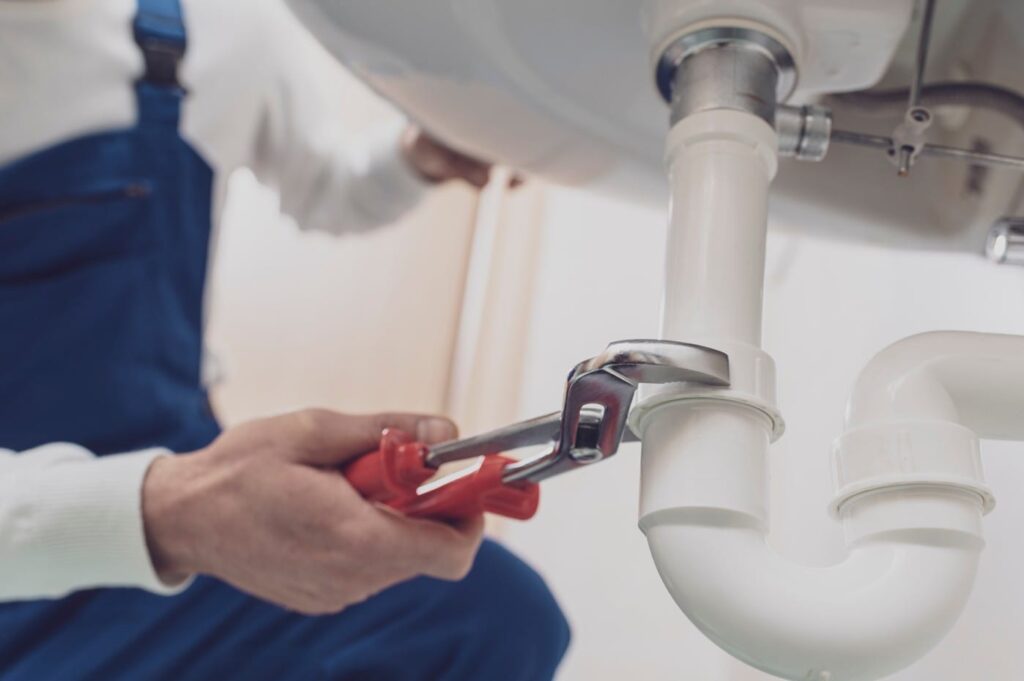 Plumber repairing a white drain pipe beneath a sink in Calhoun