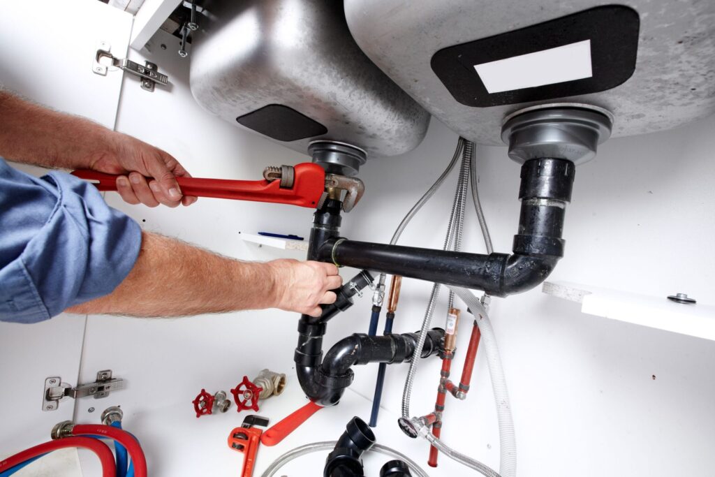 Plumber repairing drain pipes beneath a kitchen sink in Calhoun